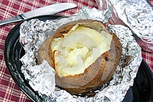 One open baked potato on aluminum foil, unwrapped.
