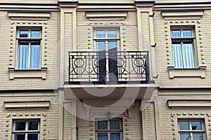 One open black iron balcony with a wrought pattern on a brown brick wall with windows