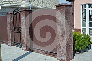 one open black metal gate and part of a brick wall of a fence on the street on a gray sidewalk