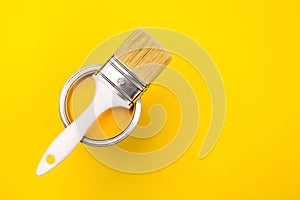 One open can of paint with white brush on it on yellow background.