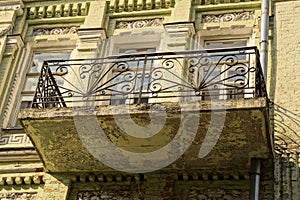 One open old balcony with black iron bars with a forged pattern on the gray concrete wall