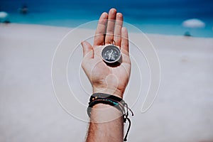 One open stretched hand palm with black metal compass on the sandy beach. Find your wish goal way concept. Blue sea in