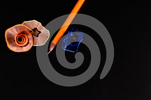 One orange pencil and a blue sharpener with waste shavings on black background