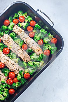 One pan dish, baked salmon fillet with broccoli and tomato on frying tray, vertical, top view