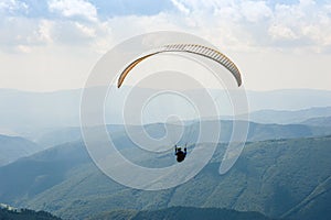 One paraglider fly over a mountain valley on a sunny summer day.