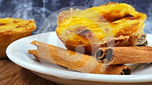 One Pastel de nata or Portuguese egg tart and cinnamon sticks on a white plate. Pastel de Belm is a small pie with a