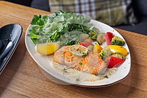 One piece of baked salmon grilled pepper lemon and salt on a brown plate with lettuce leaves. wood background