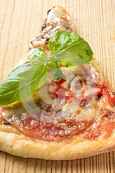 One piece of Italian pizza with tomatoes mushrooms bacon and cheese and basil leaves on wooden background cutting board