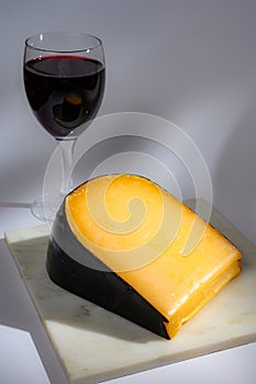 One piece of old Dutch gouda cheese with black wax and glass of red wine