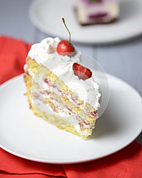 One piece of vanilla cherry cake on a white plate over light wooden background. Delicious sweet dessert close up.