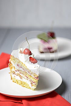 One piece of vanilla cherry cake on a white plate over light wooden background. Delicious sweet dessert close up.