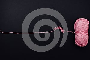 One pink cotton ball and some knitted pattern at the right side of a black background