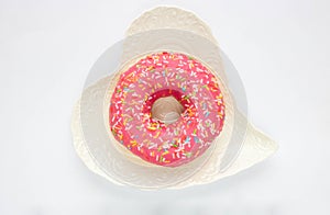 One pink sweet doughnut lies on a white heart-shaped plate on a white background