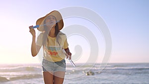 One playful woman blowing soap bubbles at the beach. Female reliving her childhood at the ocean. A young fun female