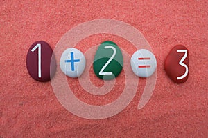 One plus two equals three, creative addition with colored stone numbers over orange sand