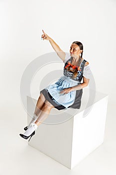 One pretty woman, waitress in traditional Austrian or Bavarian costume sitting on huge box isolated over white