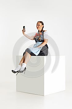 One pretty woman, waitress in traditional Austrian or Bavarian costume sitting on huge box isolated over white