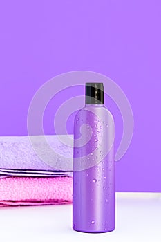 One purple cosmetic bottle and two towels on a lilac background. Spa concept