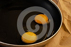 One raw egg in a black frying pan on a paper. Transparent white and bright round yellow yolk