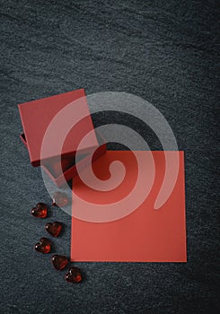 One red box, a glass heart and an empty sheet on a black stone background.