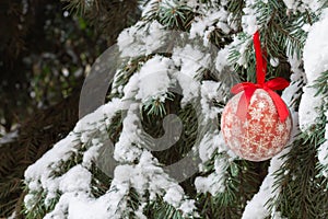 One red Christmas ball with ribbon hanging on snow Xmas tree outdoors