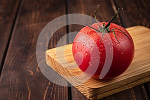 One red and fresh tomato on the wooden cutting board. raw wet vegetable with water droplets. template for advertising with copy