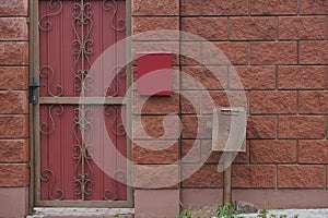 One red metal door with a wrought iron pattern and part of a brown fence wall