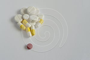 One red pill with many white and yellow pills on white background. copy space