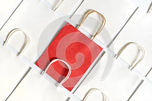 One red shopping bag in background of white bags isolated on white background.