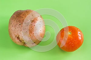 One red tomato and apotato on green background