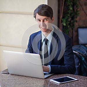 One relaxed young handsome professional businessman working with his laptop, phone and tablet in a noisy cafe.