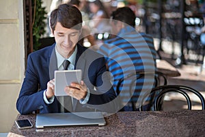 One relaxed young handsome professional businessman working with his laptop, phone and tablet in a noisy cafe.