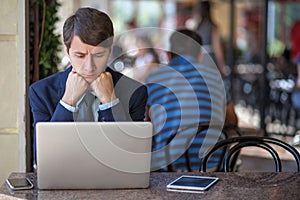 One relaxed young handsome professional businessman working with his laptop, phone and tablet in a noisy cafe.