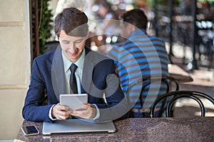 One relaxed young handsome professional businessman working with his laptop, phone and tablet in a noisy cafe.