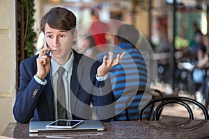 One relaxed young handsome professional businessman working with his laptop, phone and tablet in a noisy cafe.