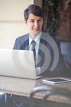 One relaxed young handsome professional businessman working with his laptop, phone and tablet in a noisy cafe.