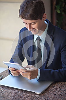 One relaxed young handsome professional businessman working with his laptop, phone and tablet in a noisy cafe.