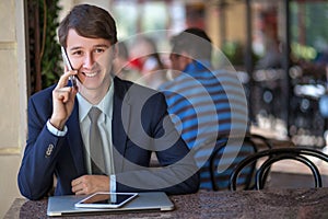 One relaxed young handsome professional businessman working with his laptop, phone and tablet in a noisy cafe.