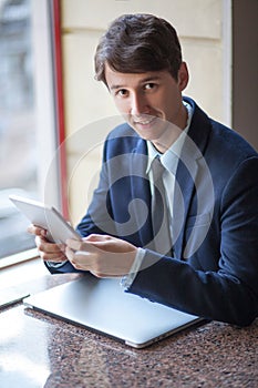 One relaxed young handsome professional businessman working with his laptop, phone and tablet in a noisy cafe.