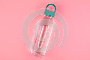 One reusable plastic water bottle with green cap at pink background. Minimalistic healthy lifestyle
