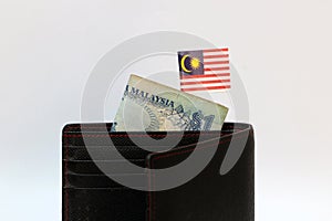 One ringgit banknote of Malaysia and mini Malaysian nation flag stick on the black wallet with white background