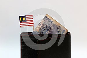 One ringgit banknote of Malaysia and mini Malaysian nation flag stick on the black wallet with white background