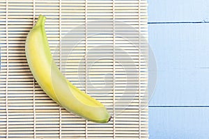 One ripe banana on bamboo mat. Top view on wooden table. Copy space