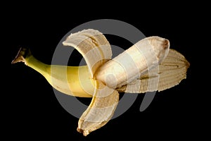 One ripe banana, half peeled, on a black background, isolated