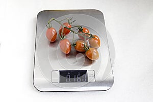 One ripe branch of cherry tomatoes is weighed on a kitchen scale