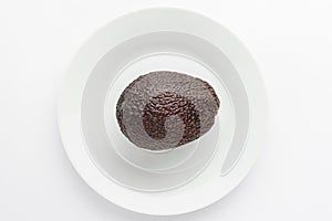 One ripe ready to eat avocado fruit on a white plate on a white table, top view