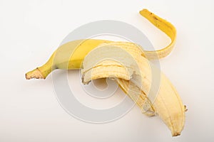 One ripe yellow partially peeled banana on a white background. Close up.