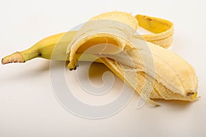 One ripe yellow partially peeled banana on a white background. Close up