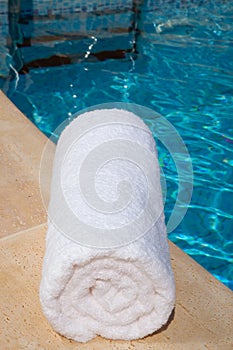 One rolled-up white towel by blue pool