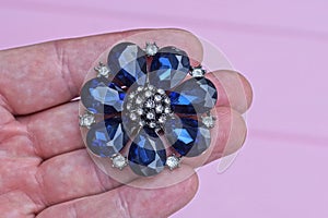 one round silver jewelry brooch in the shape of a flower with white and blue stones lies on the fingers